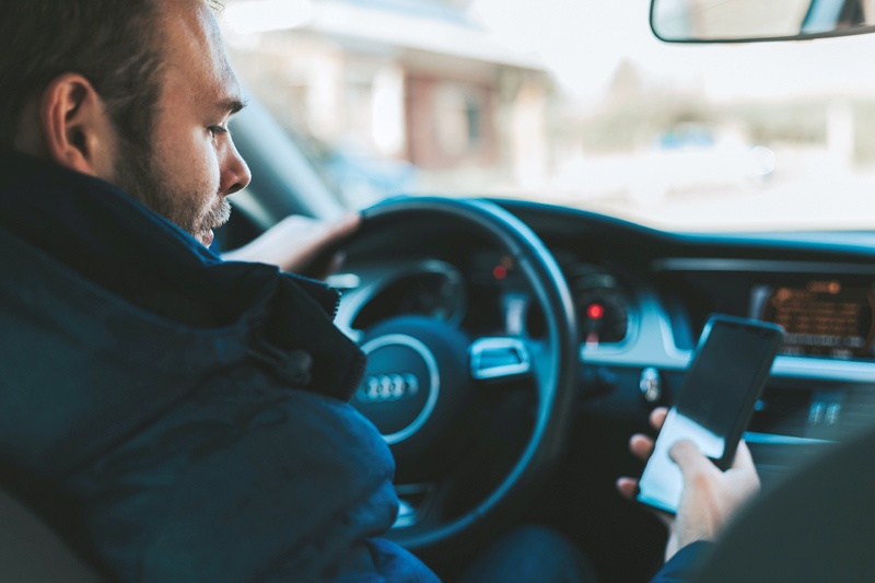 man looking at phone, ignoring oregon's distracted driving law